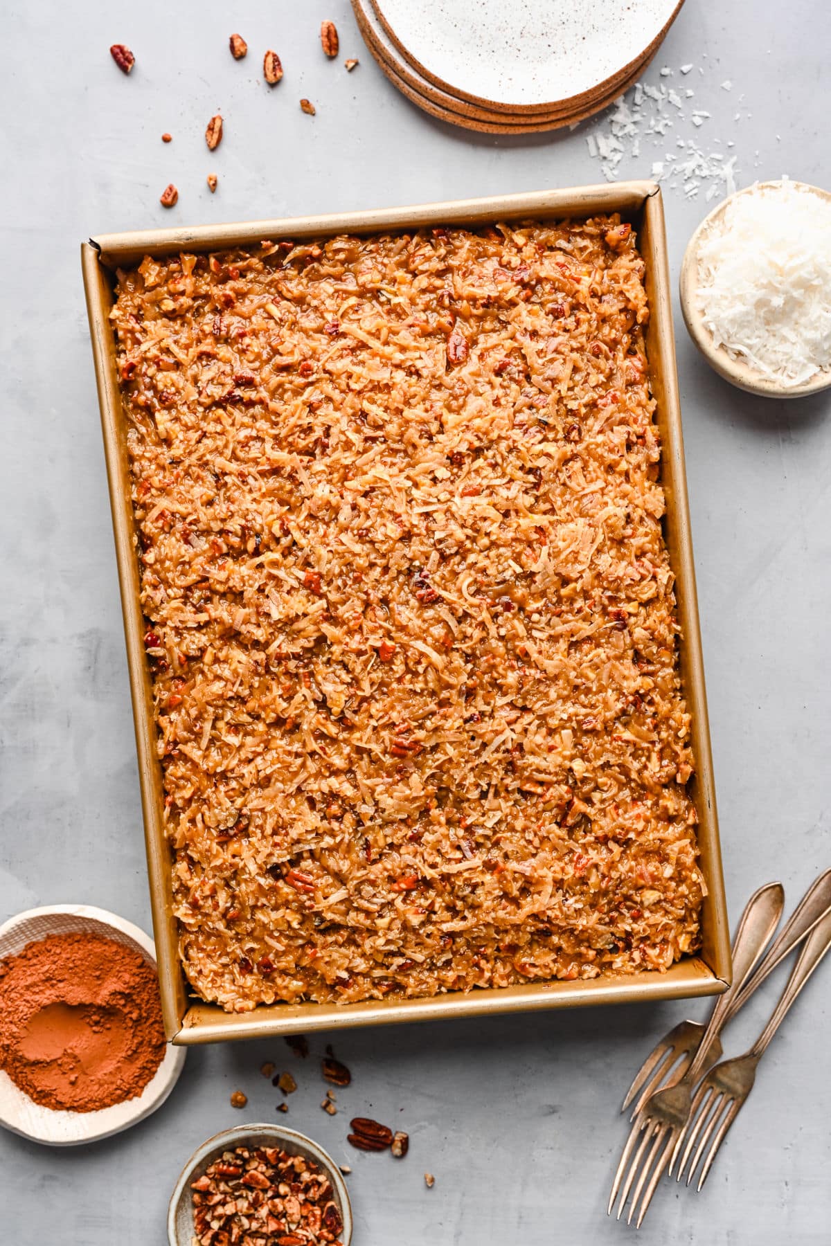 German chocolate sheet cake in the pan surrounded by forks and ingredients in dishes.