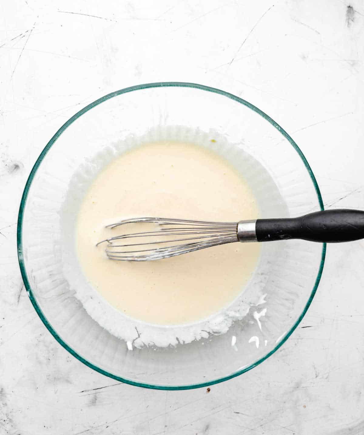 Oil milk and yogurt whisked into egg mixture in a glass mixing bowl. 