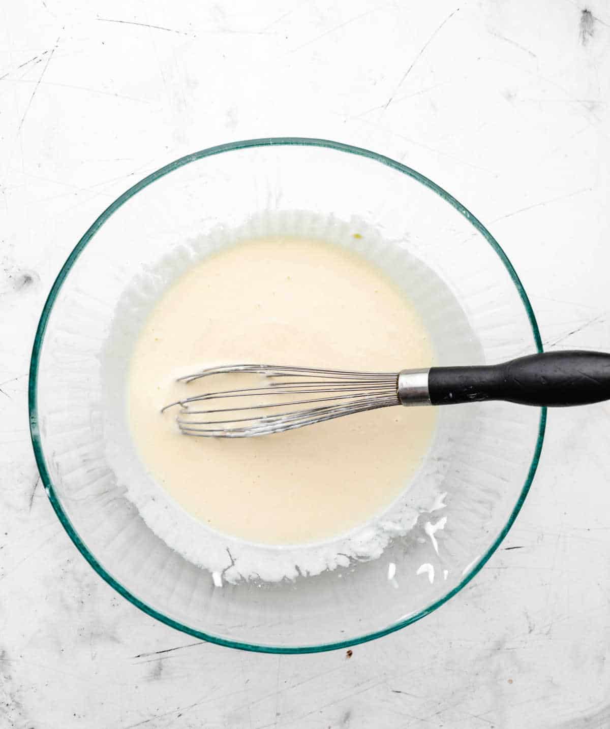 Oil milk and yogurt whisked into egg mixture in a glass mixing bowl.