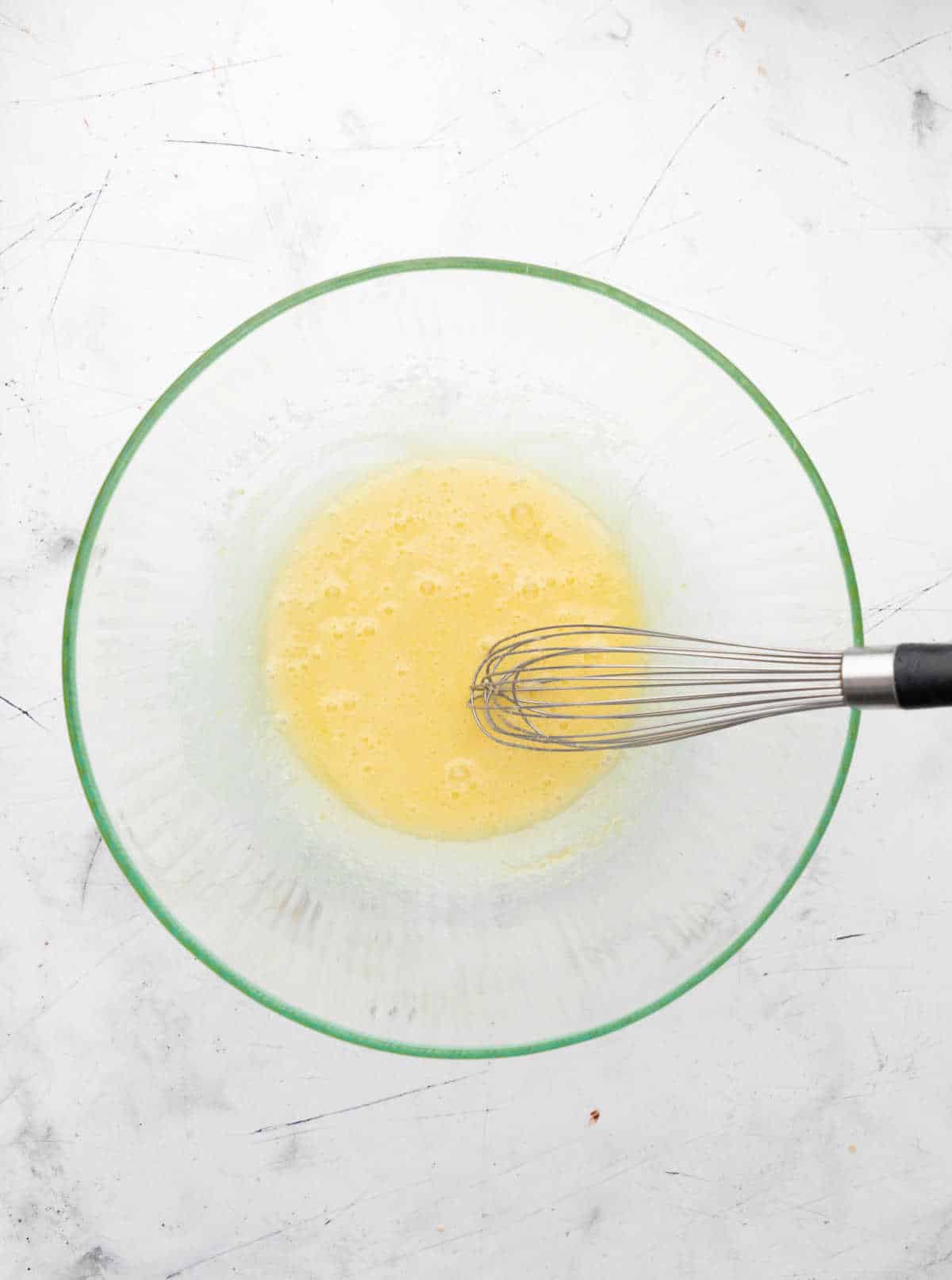 Egg and sugar whisked together in a glass mixing bowl.