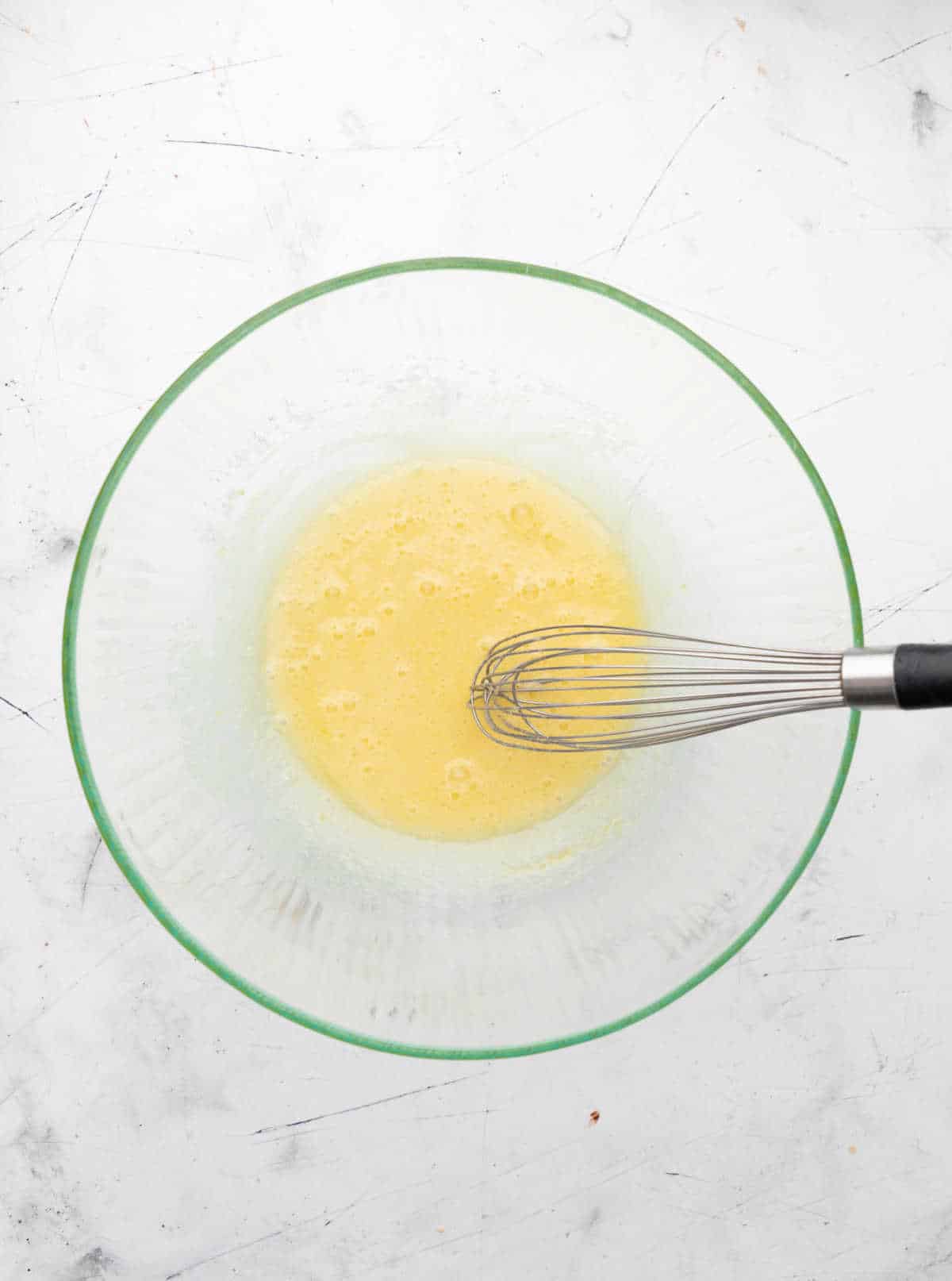 Egg and sugar whisked together in a glass mixing bowl. 