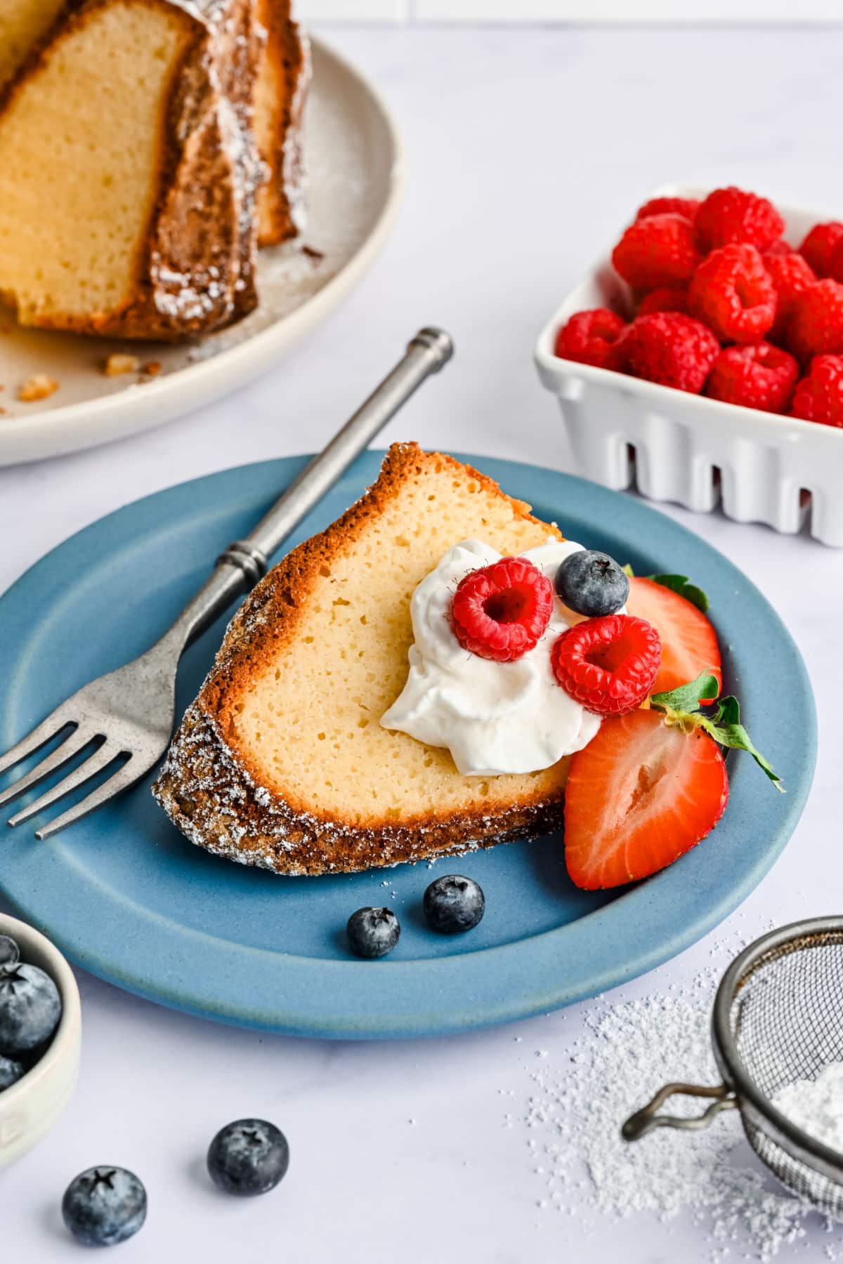 A slice of Greek yogurt pound cake topped with fresh whipped cream and berries.