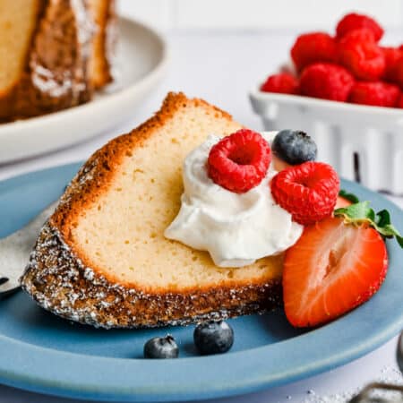 A slice of Greek yogurt pound cake on a blue plate next to a bowl of raspberries.