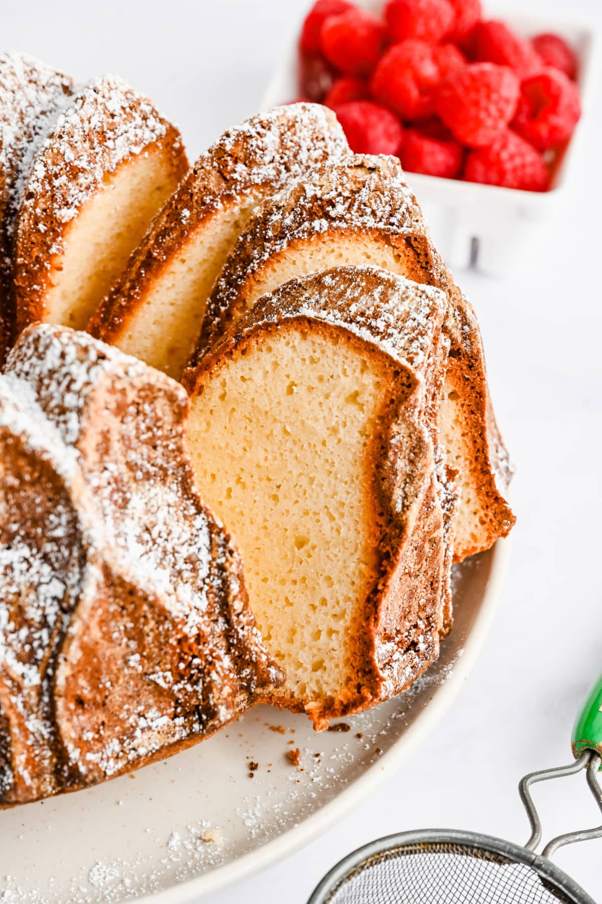 Slices of Greek yogurt pound cake next to a dish of raspberries. 