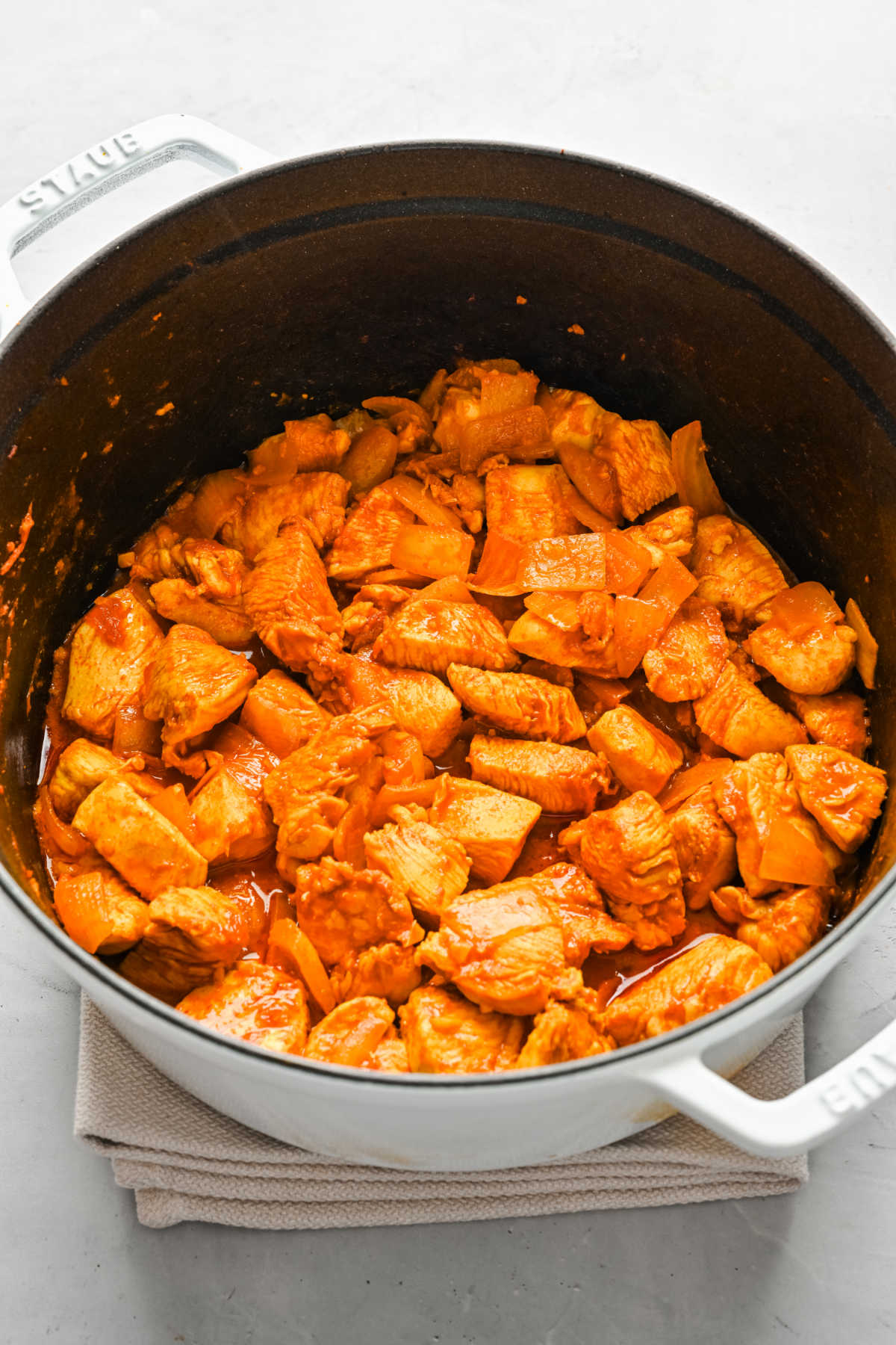 Chicken pieces sauteing with curry paste in a pot.