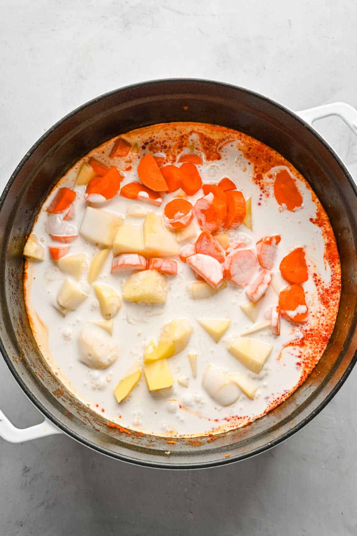 Carrot potato and coconut milk in curry mixture in a pot.