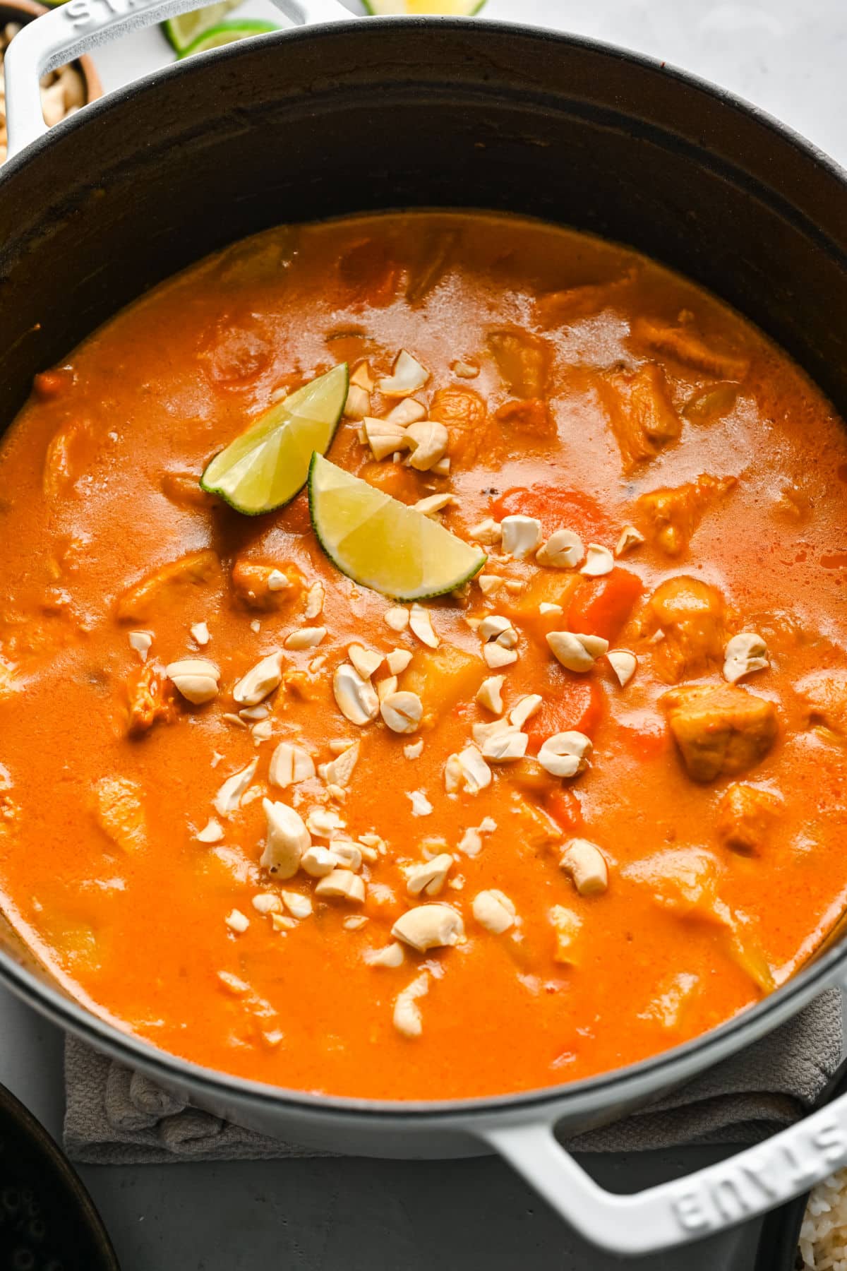A pot of chicken massaman curry topped with peanuts and lime slices.