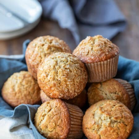 A basket of oatmeal muffins next to a stack of white plates.