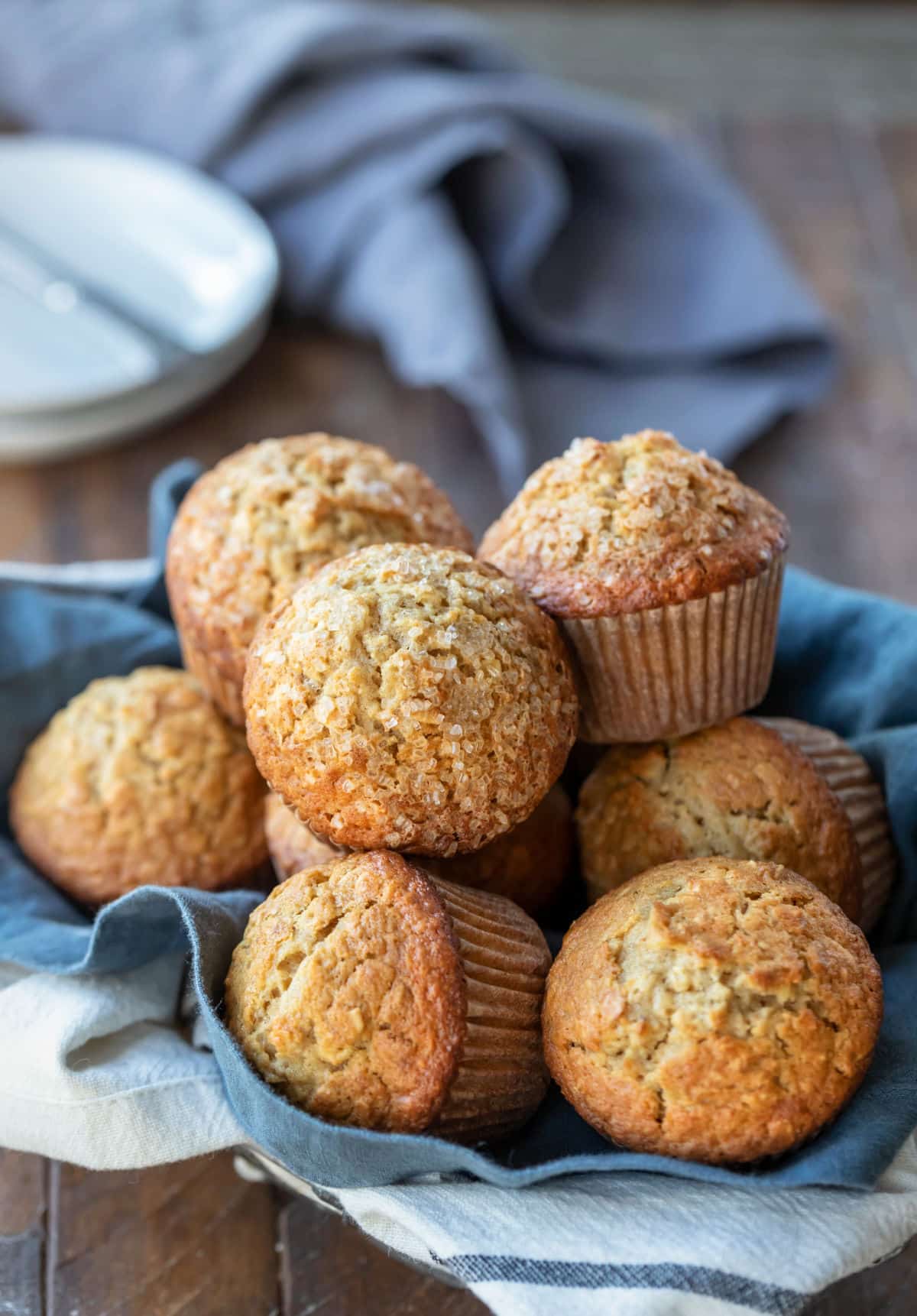 A basket of oatmeal muffins next to a stack of white plates.