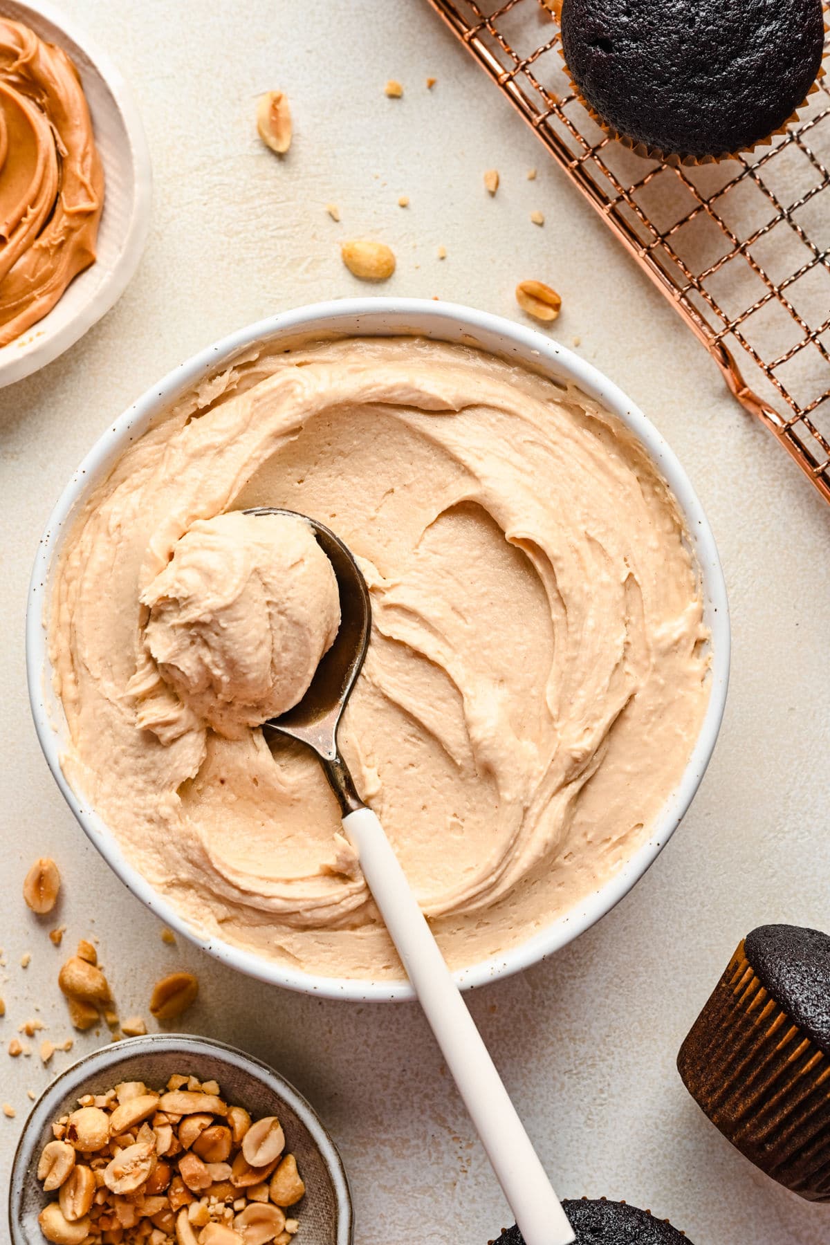 A spoon scooping up peanut butter frosting in a white dish.
