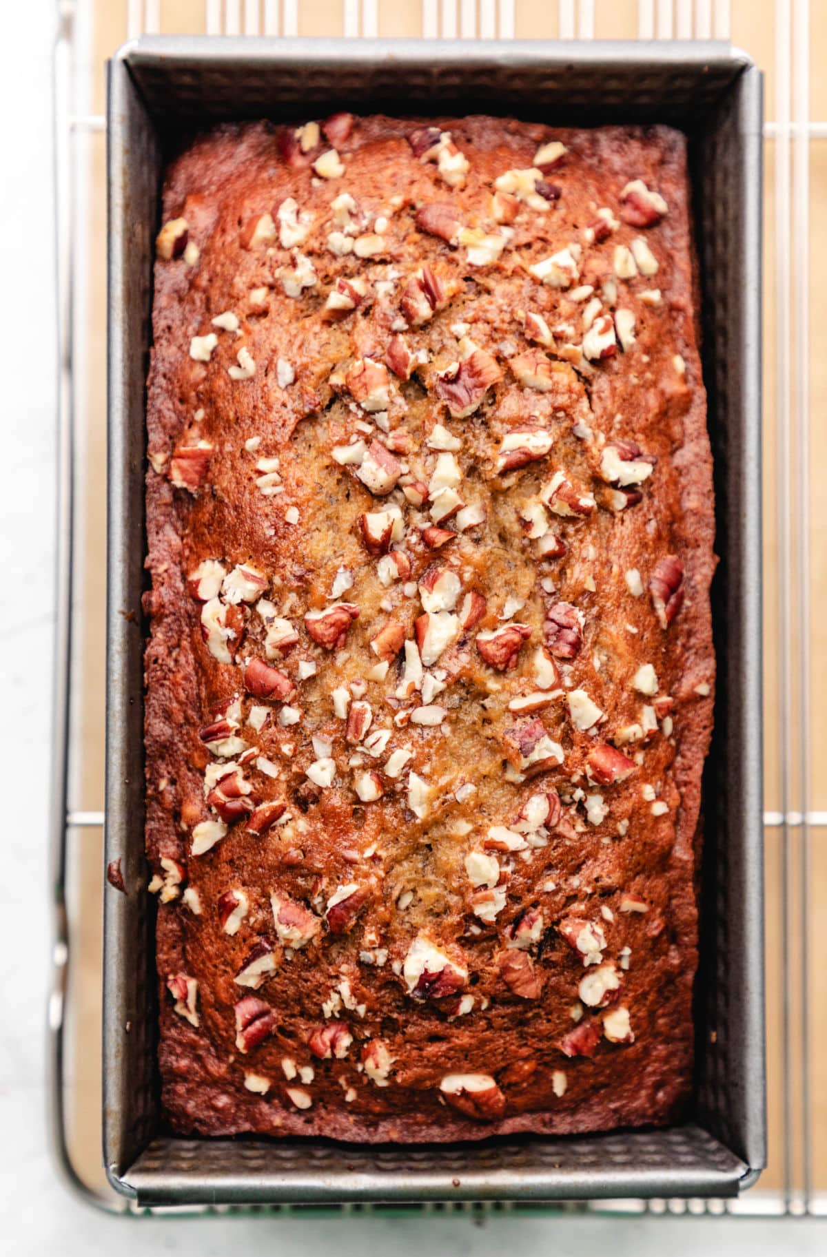 A loaf of banana nut bread in the pan on a wire cooling rack.