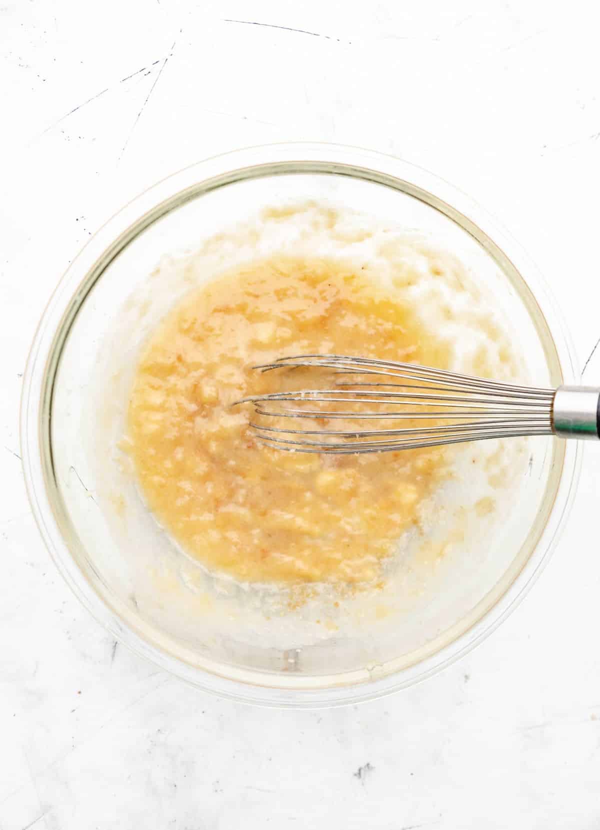 Mashed bananas and melted butter whisked together in a glass mixing bowl. 
