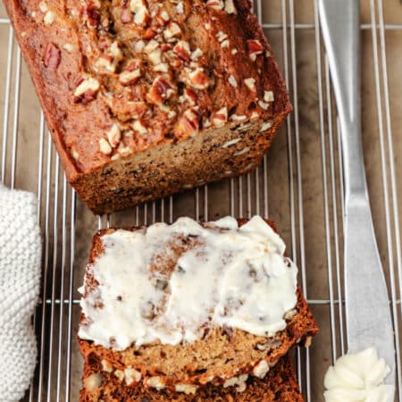 A half buttered slice of banana nut bread next to the loaf.