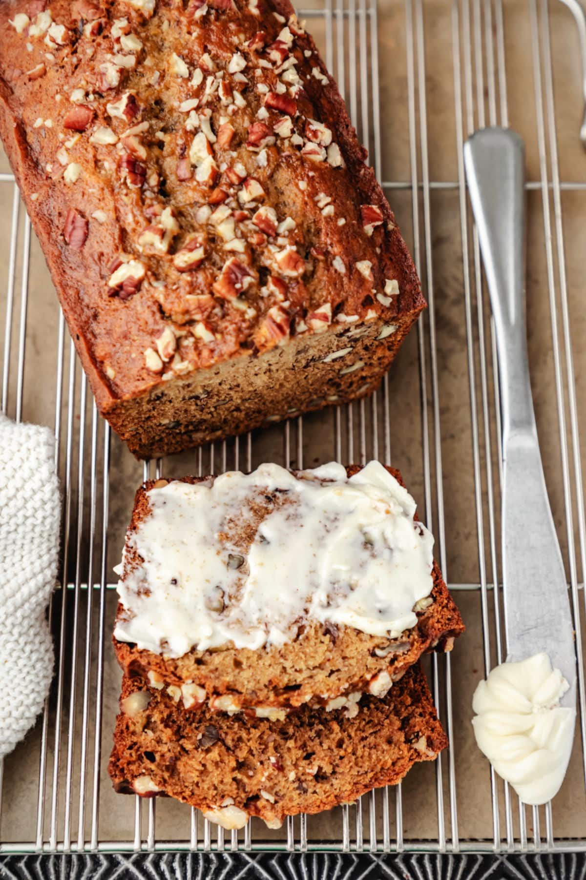 A half buttered slice of banana nut bread next to the loaf. 