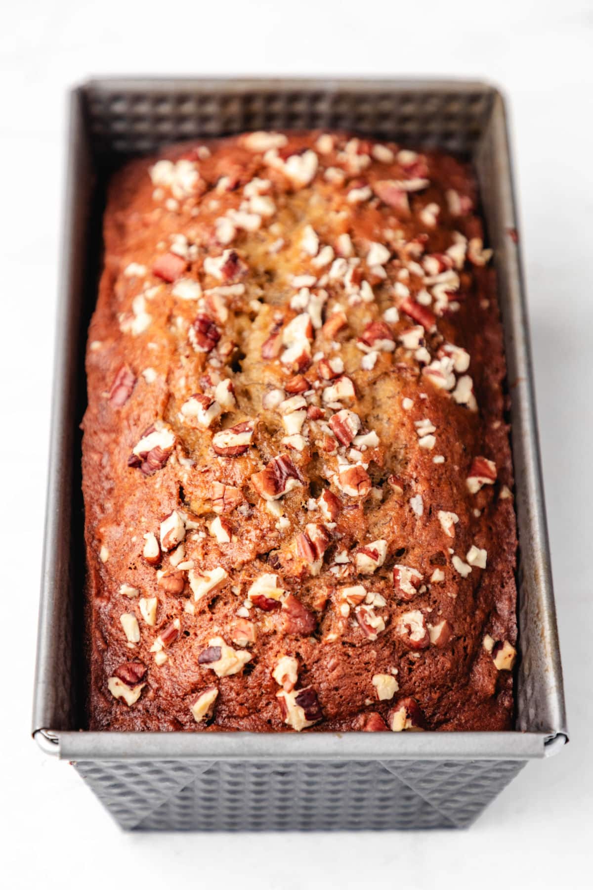 A loaf of banana nut bread in a metal loaf pan.