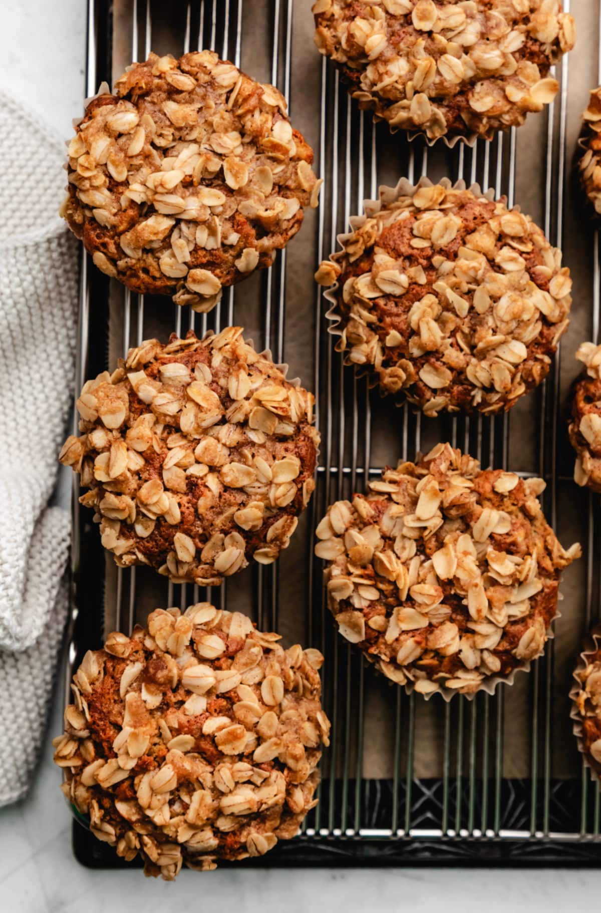 Two rows of banana oatmeal muffins next to a cream knit dish towel. 