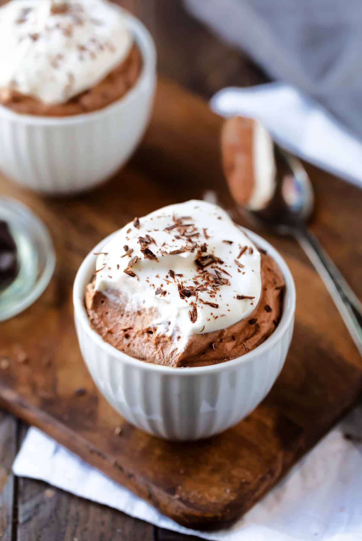 Two cups of chocolate mousse with a spoon holding a bite. 