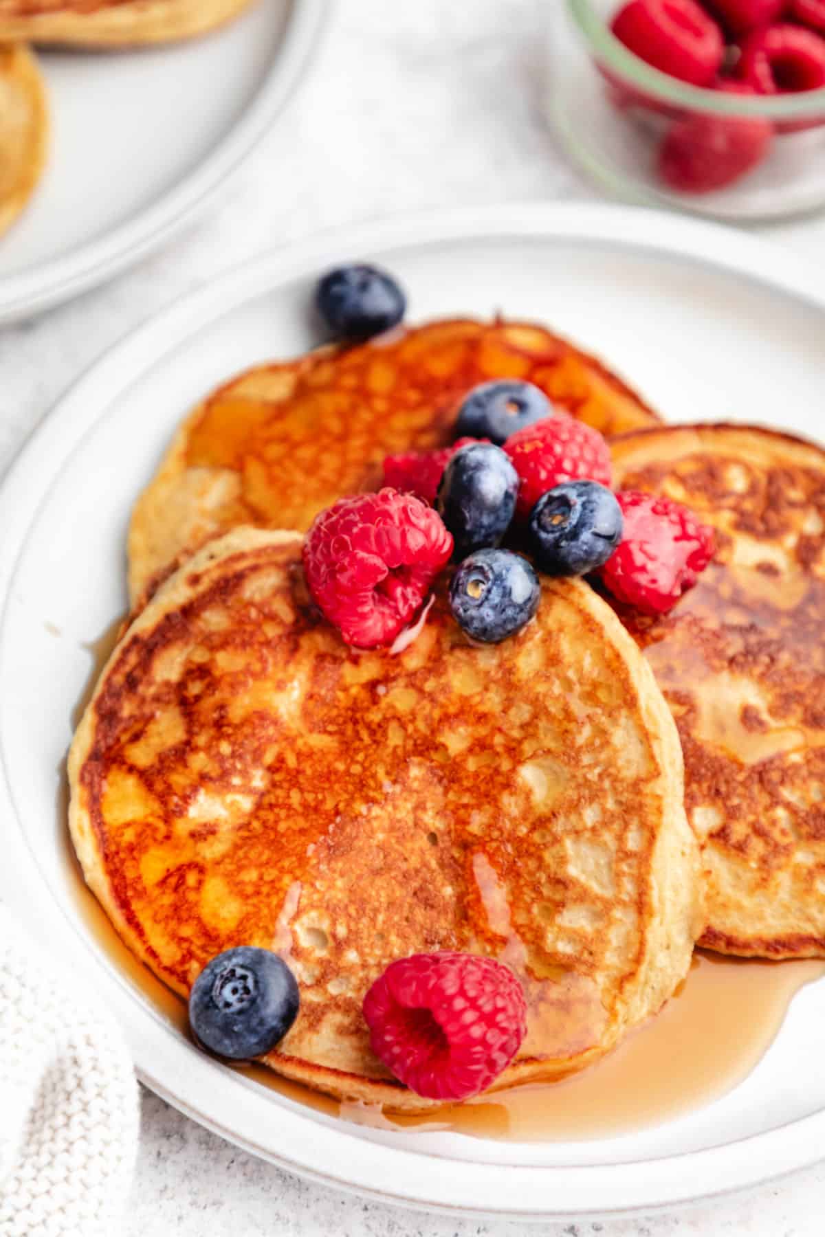 A plate of cottage cheese pancakes next to a dish of raspberries.