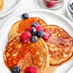 A plate of cottage cheese pancakes next to bowls of raspberries and blueberries.