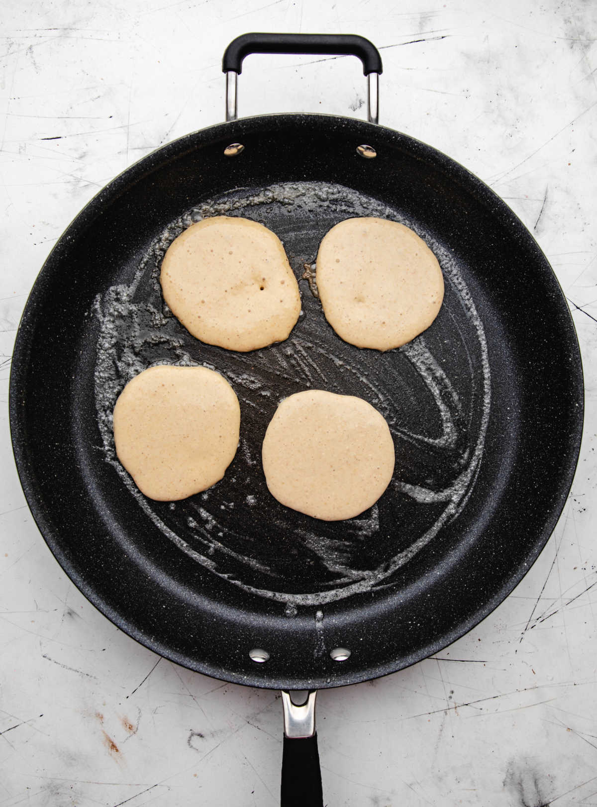 Four cottage cheese pancakes cooking in a skillet.