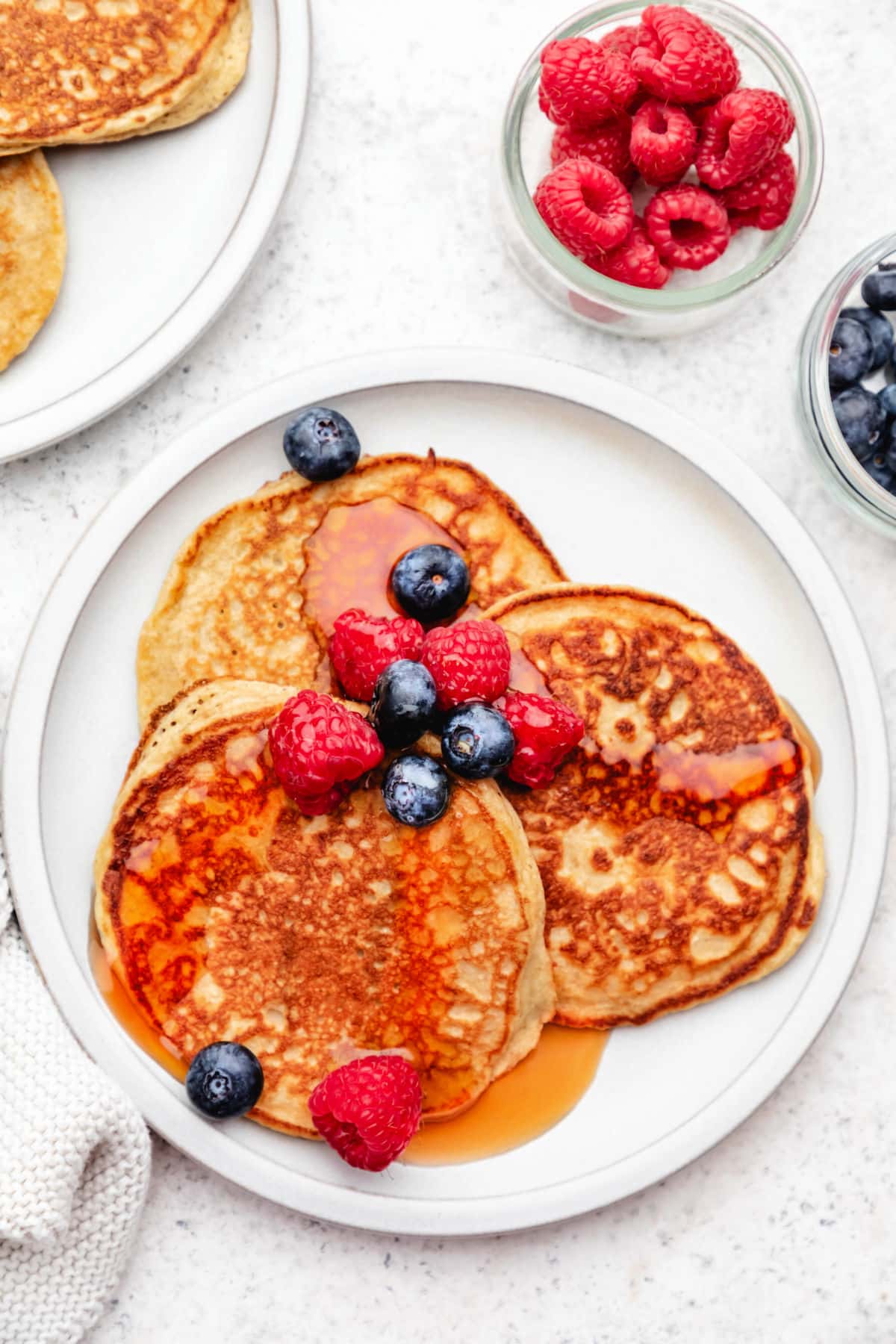 A plate of three cottage cheese pancakes topped with blueberries and raspberries.