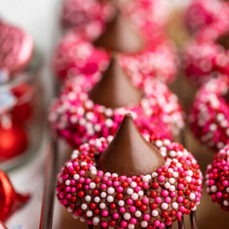 A row of Valentine's Day kiss cookies next to pink and red Hershey kisses.