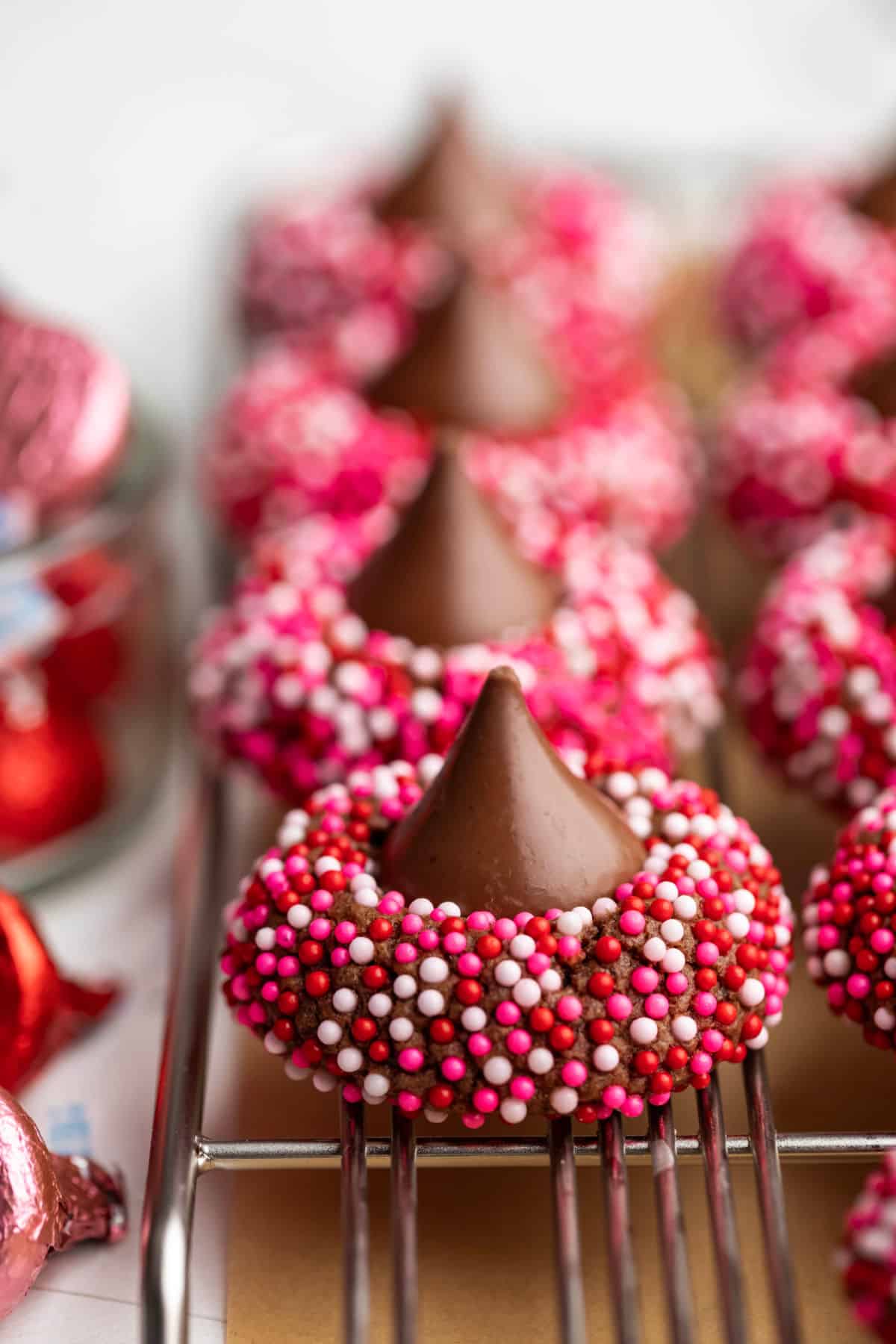A row of Valentine's Day kiss cookies next to pink and red Hershey kisses.