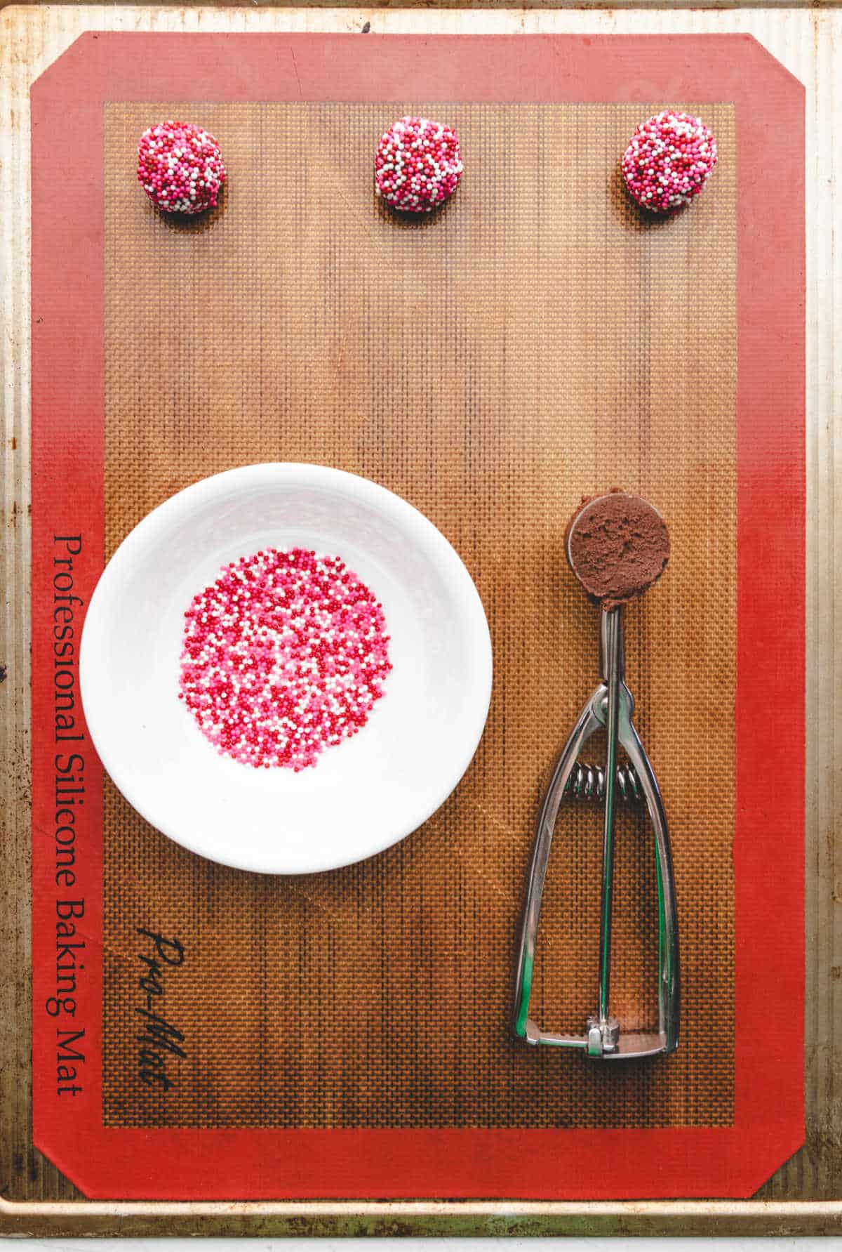 A dish of Valentine's Day sprinkles next to a cookie scoop full of dough.
