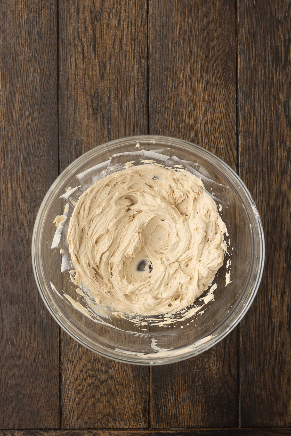 Cream cheese beaten together with vanilla extract in a glass mixing bowl.
