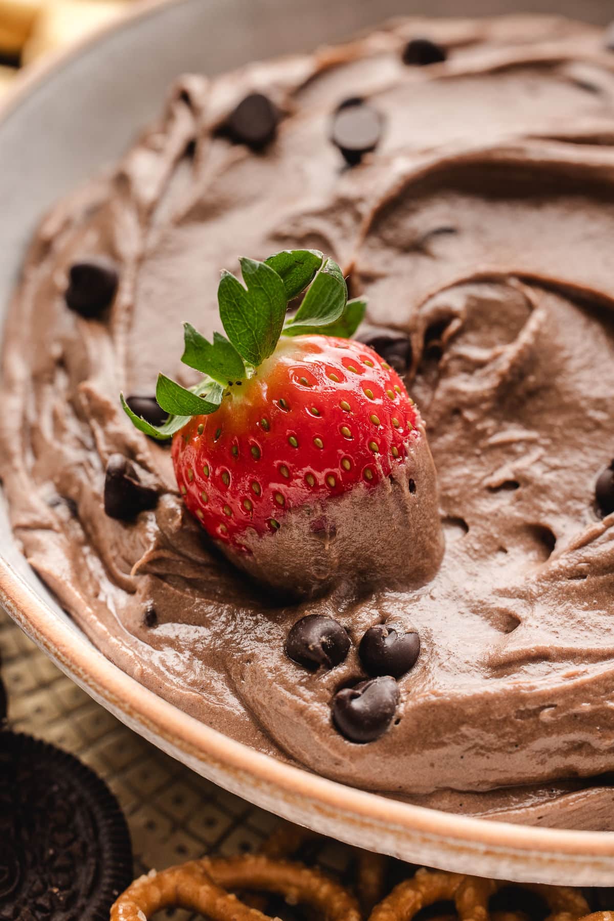 A strawberry sitting in a dish of brownie batter dip.