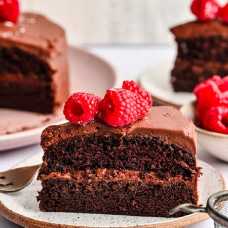 A slice of chocolate brownie cake on a plate topped with fresh raspberries.