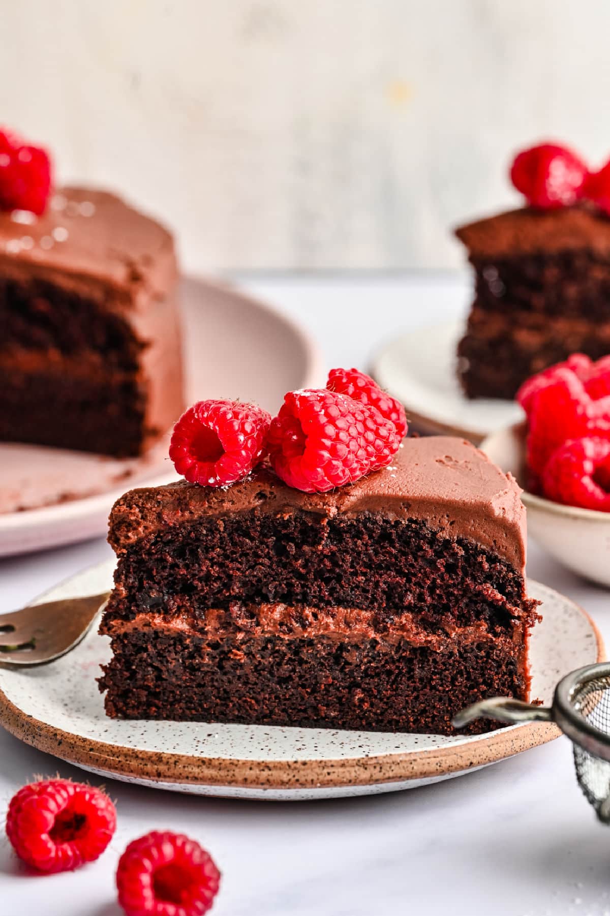 A slice of chocolate brownie cake on a plate topped with fresh raspberries.