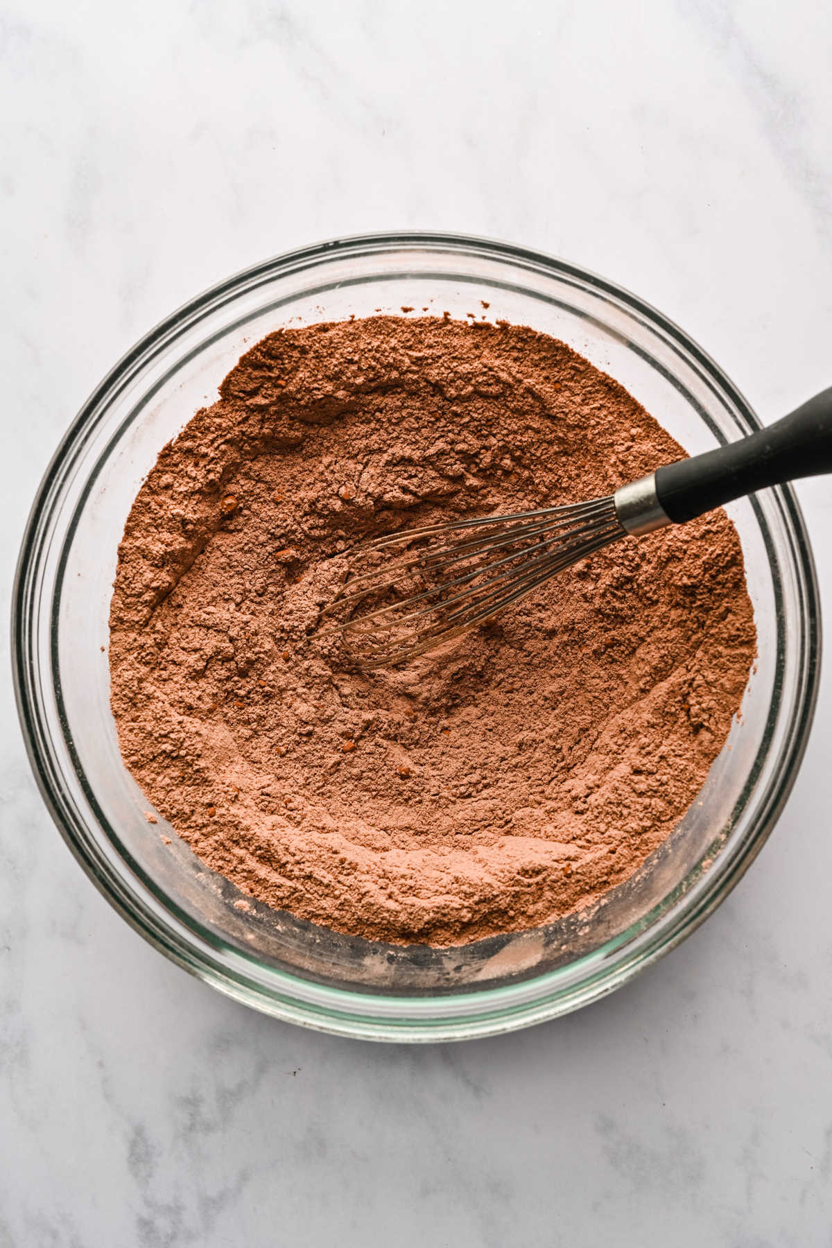 Dry ingredients for chocolate brownie cake in a glass mixing bowl. 