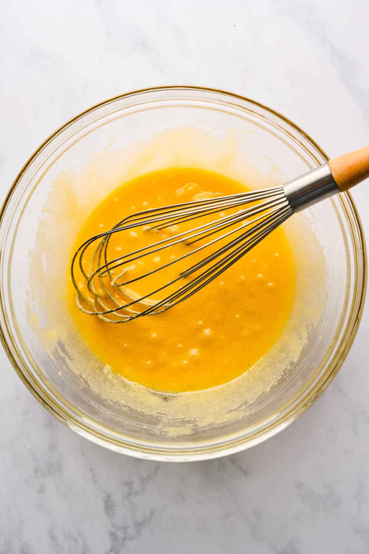 Egg mixture in a glass mixing bowl with a whisk in it.