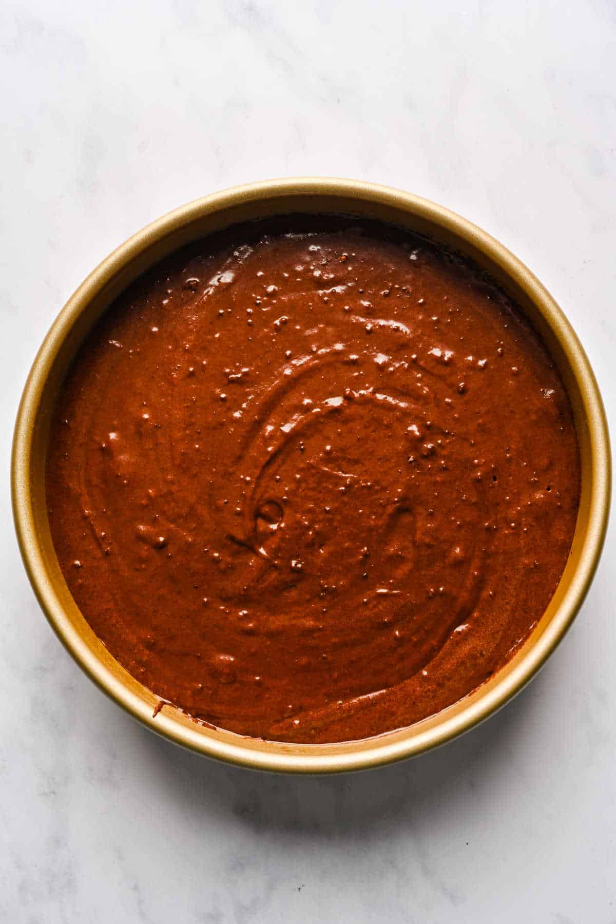 Chocolate brownie cake batter in a round cake pan.