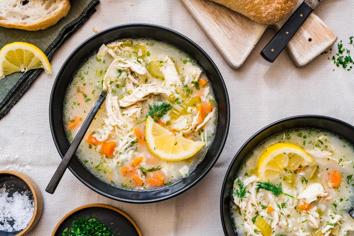 A bowl of lemon chicken and rice soup with a sliced lemon on the side.