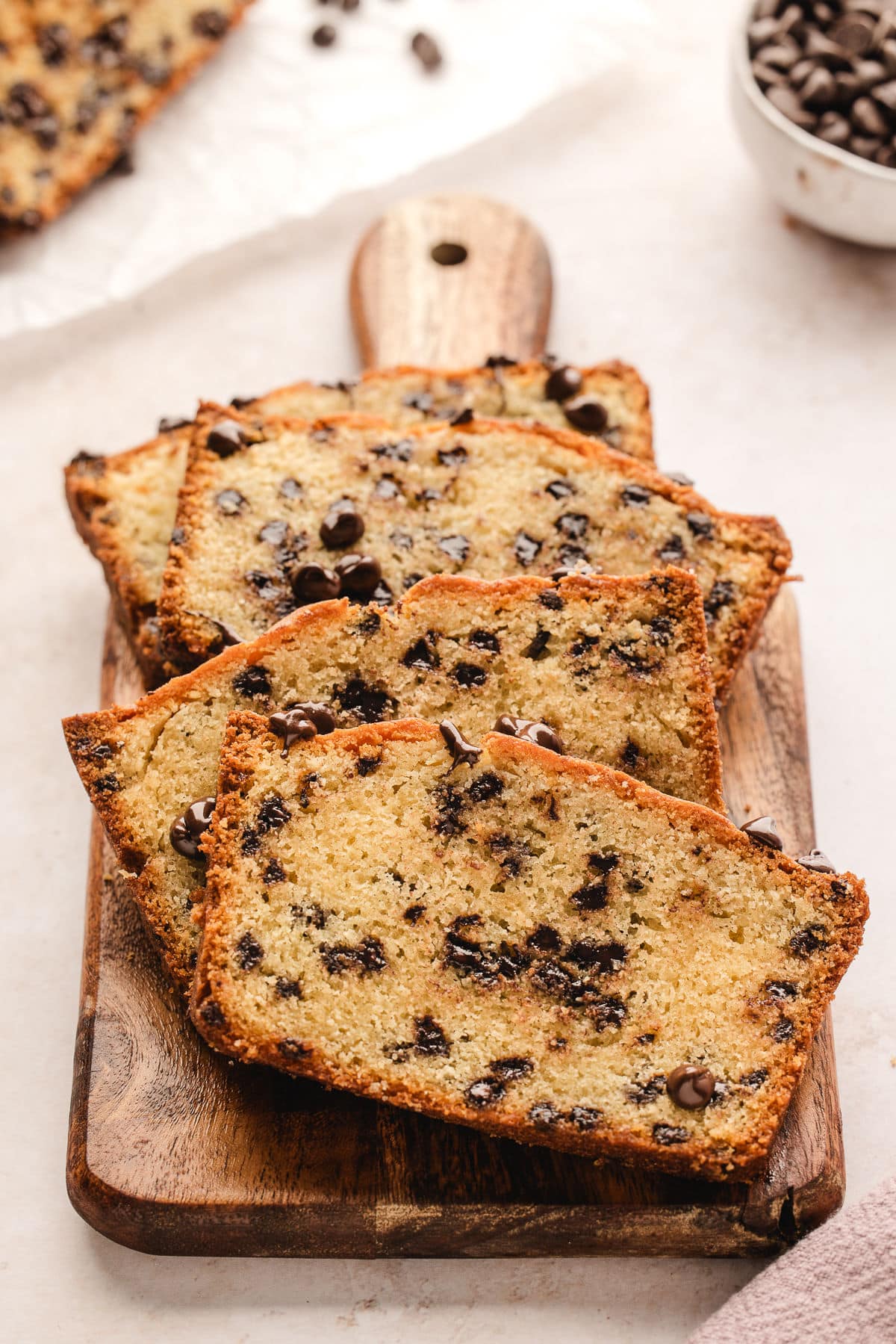 Slices of chocolate chip loaf cake on a wooden cutting board.