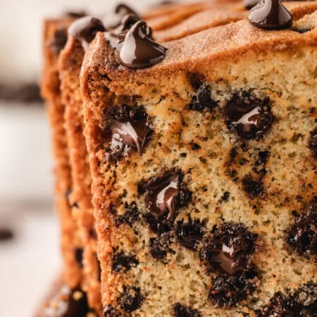 Upright slices of chocolate chip loaf cake on a wooden cutting board.