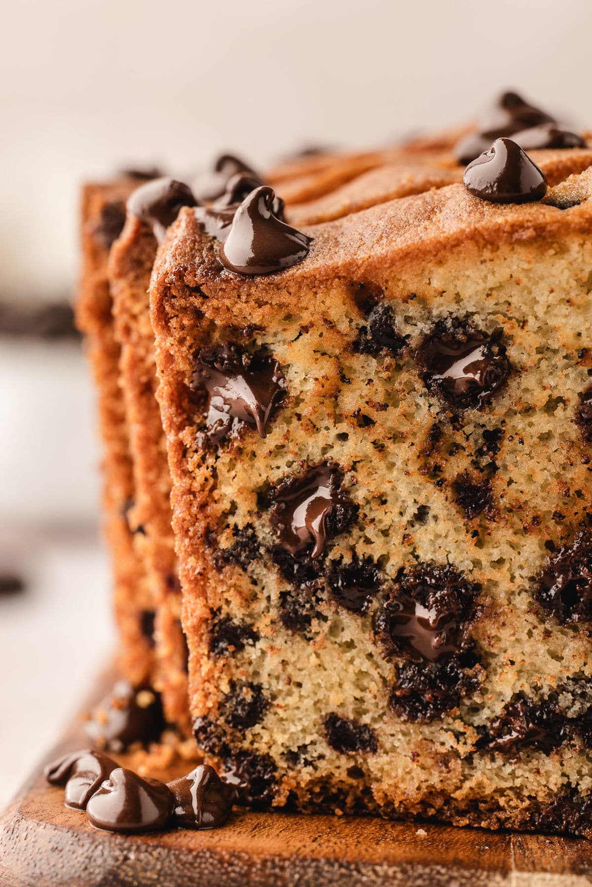 Upright slices of chocolate chip loaf cake on a wooden cutting board. 