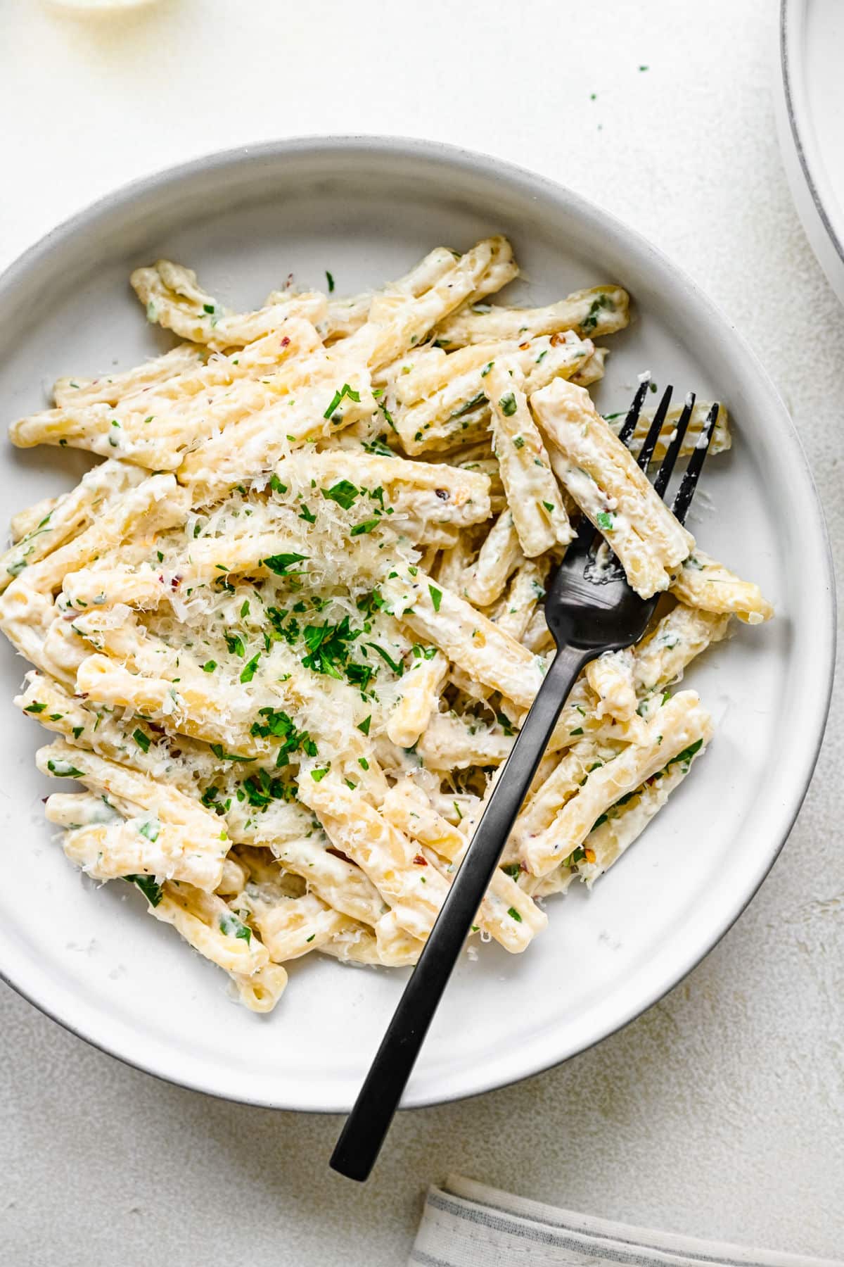 A plate of cream cheese pasta with a black fork in it.