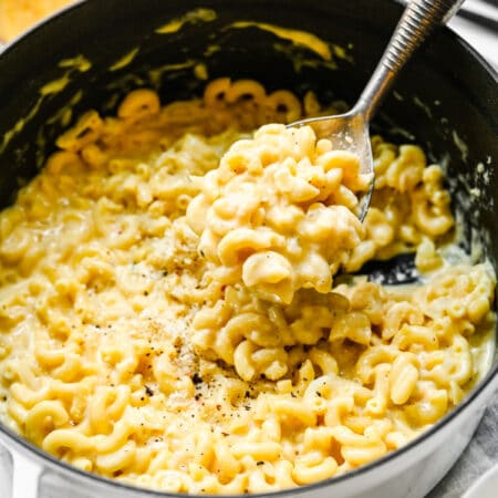 A hand holding a spoon with a scoop of gouda mac and cheese on it.