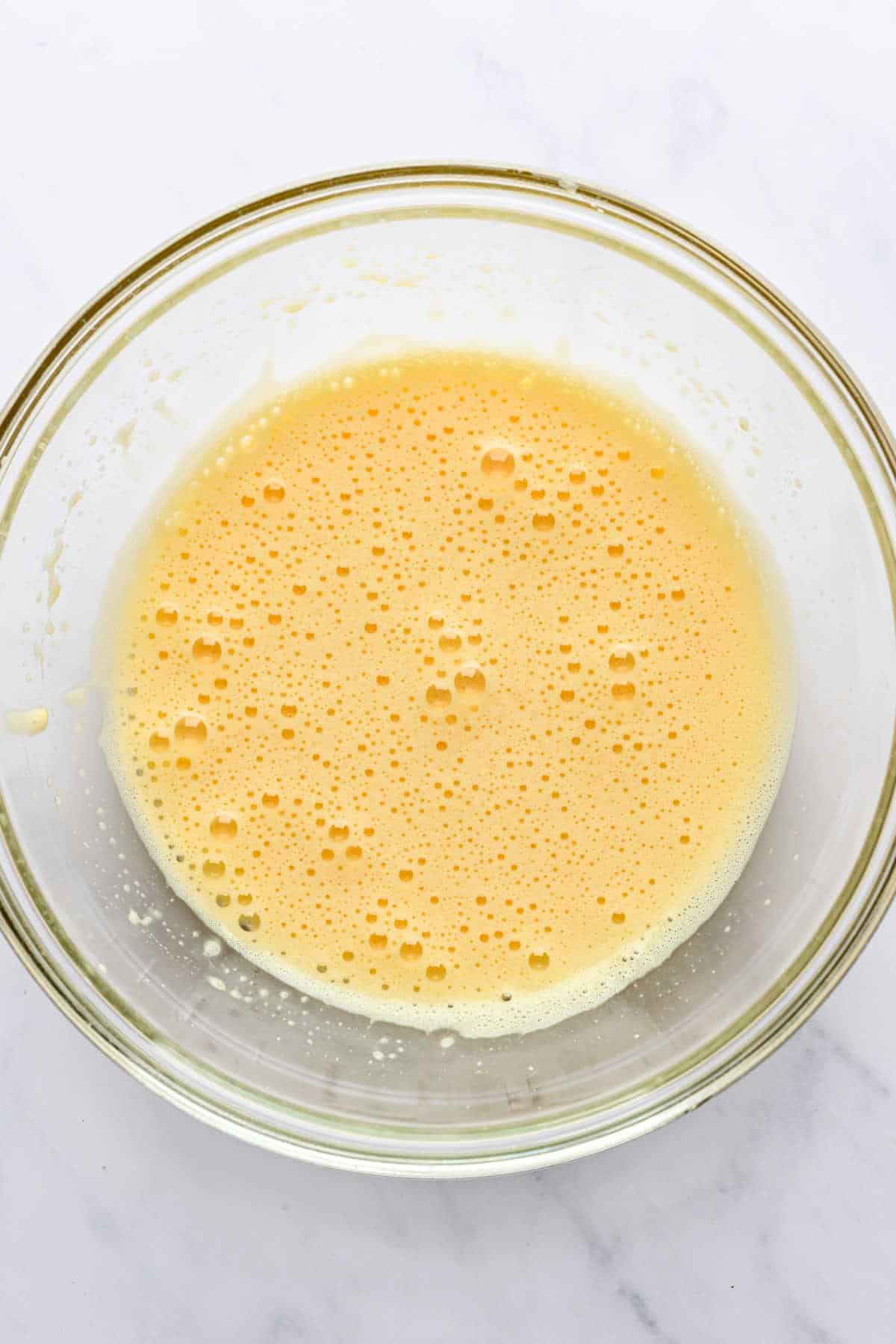 Beaten egg and egg yolks in a glass mixing bowl.