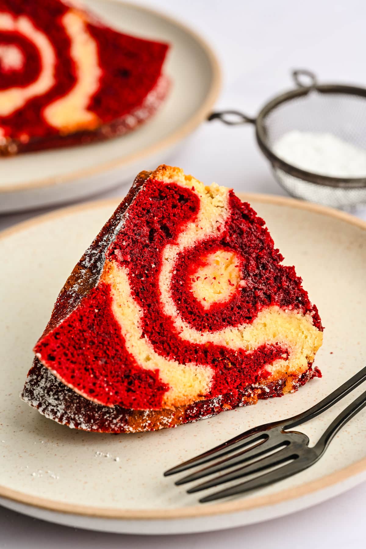A slice of red velvet marble cake on a plate wiht a fork. 