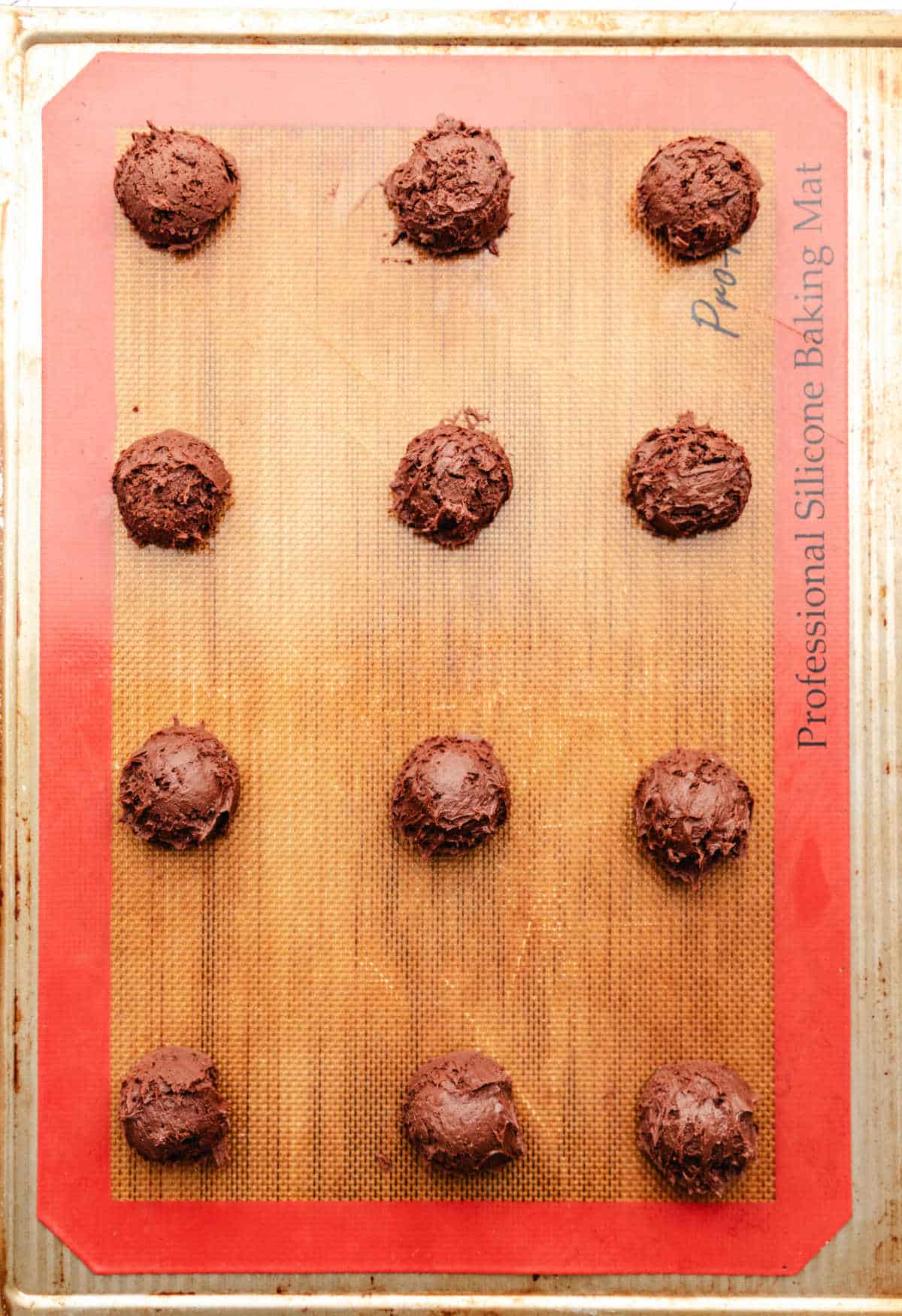 Scoops of brownie cookie dough on a silicone lined baking mat. 