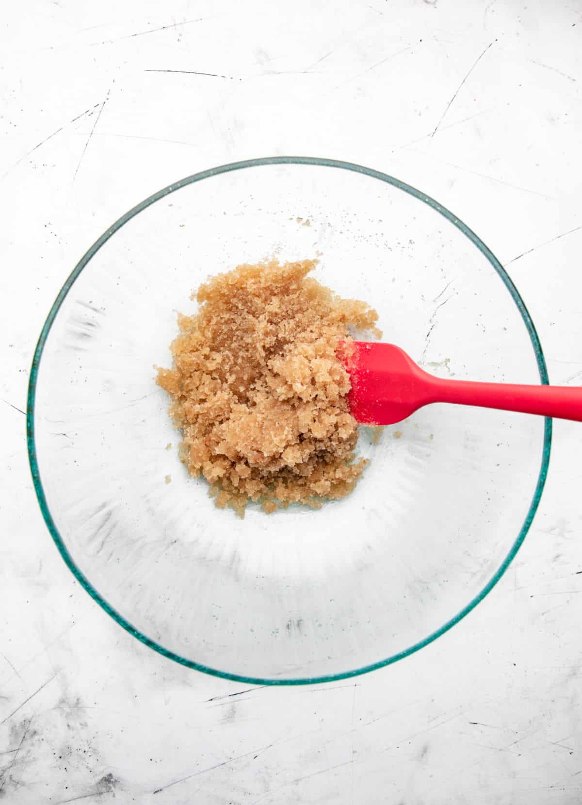 Oil and sugars mixed together in a glass mixing bowl.