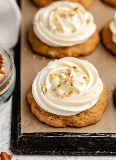 A row of carrot cake cookies topped with cream cheese frosting and chopped pecans.