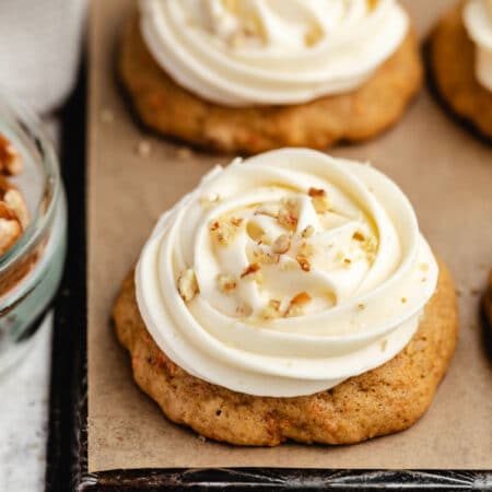 A row of carrot cake cookies topped with cream cheese frosting and chopped pecans.