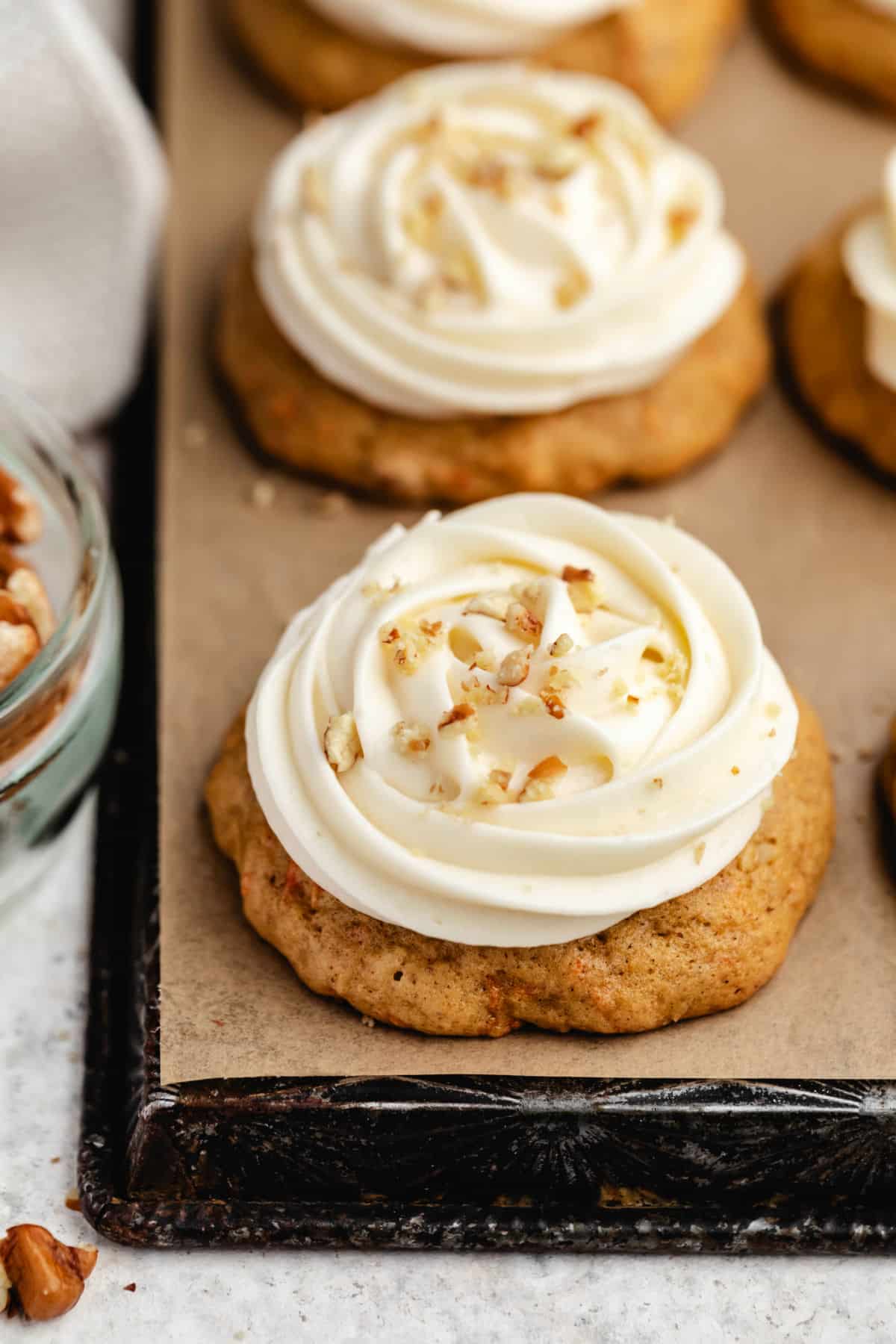 A row of carrot cake cookies topped with cream cheese frosting and chopped pecans.