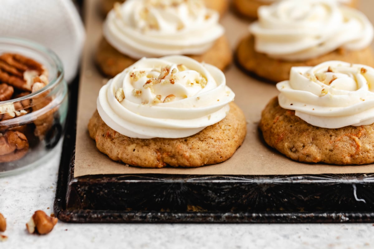 Rows of frosted carrot cake cookies on a piece of brown parchment paper. 