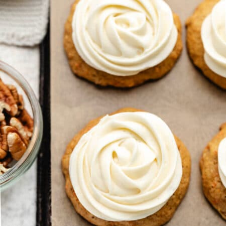 A row of carrot cake cookies topped with cream cheese frosting piped in a rosette.